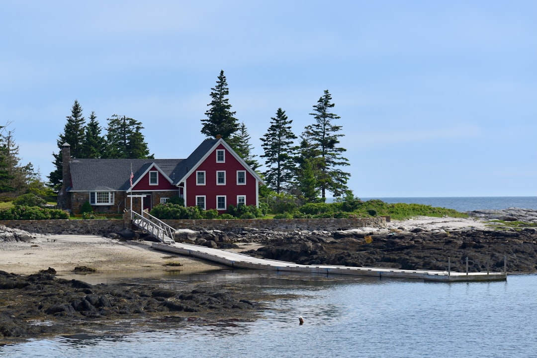 Illustration showing two Maine house build budgets side-by-side with line items like sitework, foundation, framing, MEP, finishes, and permits